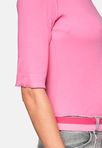 Pink short-sleeve top with a ribbed texture and scalloped sleeve edges, paired with gray denim, featuring a pink striped waistband.
