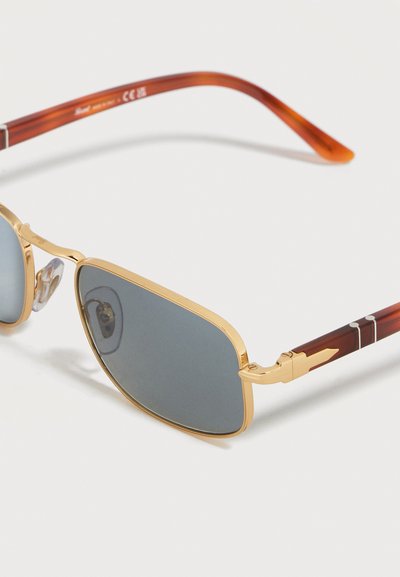 Ορθογώνια γυαλιά ηλίου με χρυσό πλαίσιο, σκούρους φακούς και βραχίονες με σχέδιο χελώνας, με μικρή χρυσή λεπτομέρεια σε σχήμα βέλους κοντά στις μεντεσέδες.