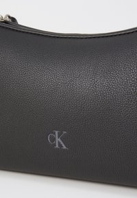 Čierna peňaženka z textúrovaného kože s hladkým zipsom, na povrchu je jemne embosované logo "cK". Kompaktný, zaoblený dizajn.