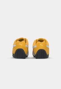 Gelbe Wildleder- und graue synthetische Rückseite eines Sneakers mit strukturiertem schwarzem Gummisohle. Verfügt über das markante PUMA-Logo an der Ferse.