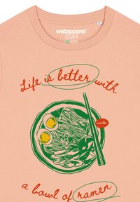 Perzikkleurig T-shirt met een groen ramenkom graphic, gele eieren, eetstokjes en rode tekst: "Het leven is beter met een kom ramen."