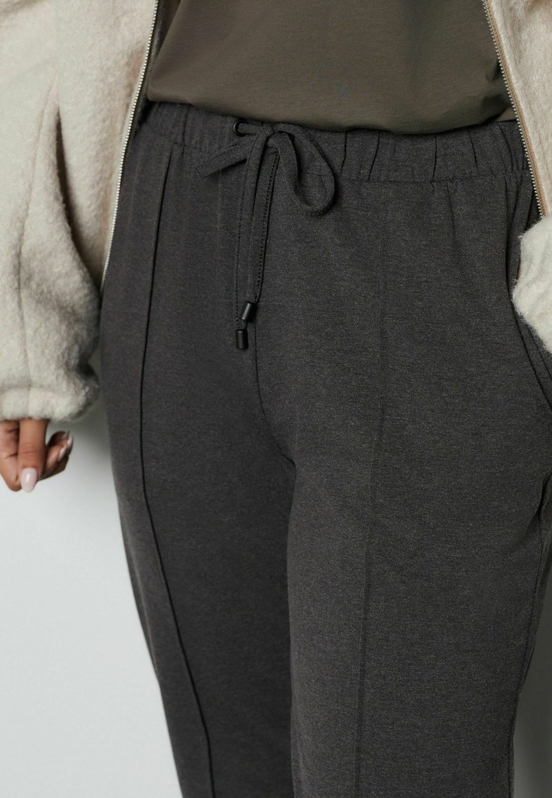 Šedé teplákové nohavice vyrobené z jemnej látky, s elastickým pásom na šnúrku a bočnými vreckami pre pohodlie.