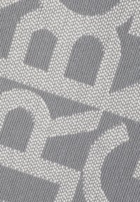 Tessuto tessuto grigio con un motivo geometrico in grigio chiaro e bianco. La texture è ruvida con sovrapposizioni distinte e forme in contrasto.