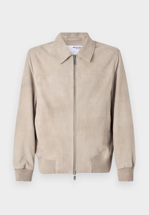 Beige velúr dzseki, gallérral, elülső cipzárral és bordázott mandzsettákkal. Minimalista varrás és két oldalzseb jellemzi. Simaság.