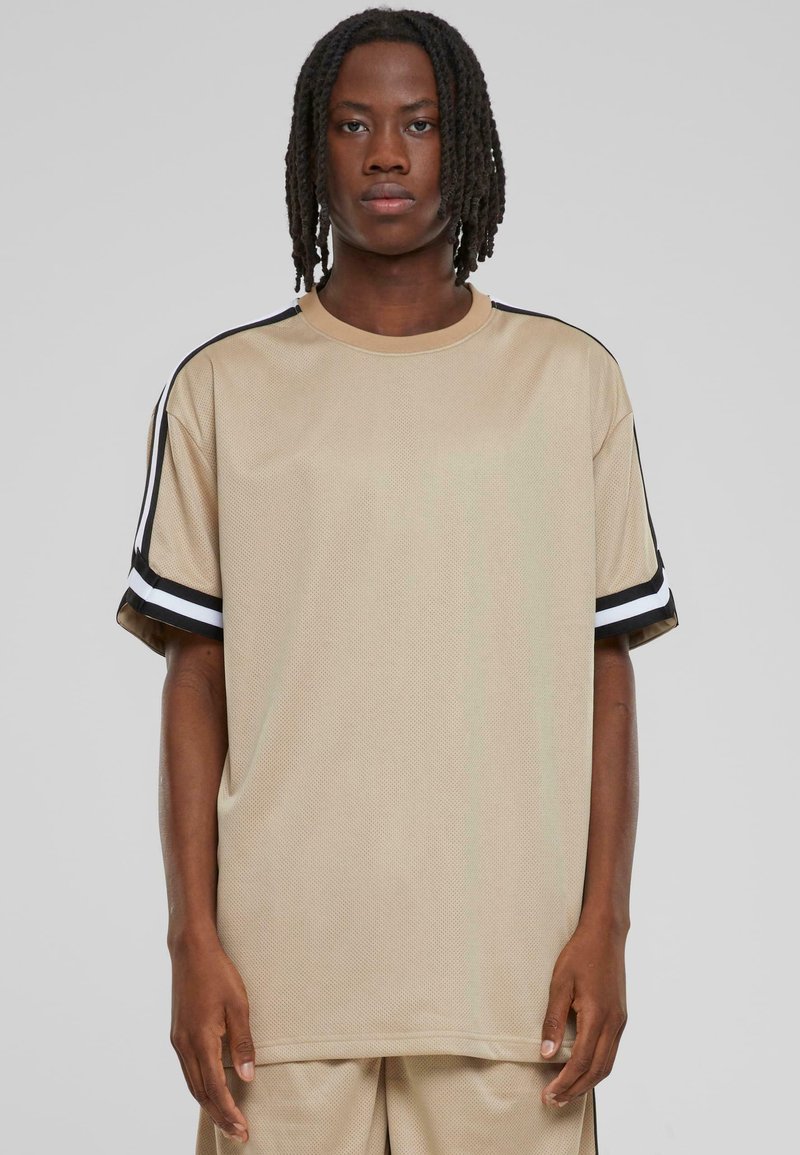 Beige oversized tričko z mřížkované látky, s černobílými pruhovanými detaily na rukávech. Kulatý výstřih a uvolněný střih.