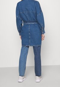 Denimklänning med långa ärmar, bälte i midjan och detaljer vid ryggen. Buren med tvåfärgade jeans och vita sneakers.