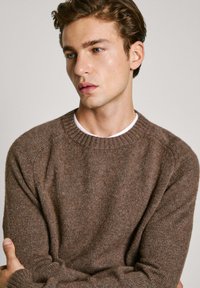 Suéter de punto marrón con un cuello redondo acanalado y mangas raglán. La textura parece suave y acogedora, con sutiles variaciones de color.