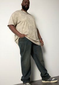 Beige mønstrede oversized t-shirt, løse blå jeans og grå sneakers med hvide detaljer. Viser et afslappet fit og teksturerede materialer.
