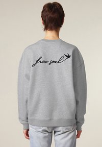 Felpa grigia con vestibilità oversize, caratterizzata da testo ricamato nero "free soul" e un design di una rondine sul retro. Polsini e orlo a costine.