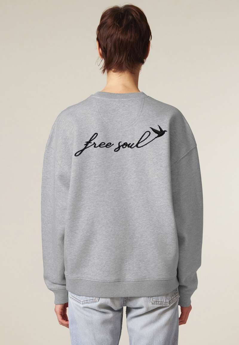 Felpa grigia con vestibilità oversize, caratterizzata da testo ricamato nero "free soul" e un design di una rondine sul retro. Polsini e orlo a costine.