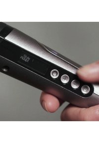 Sølvhåndholdt enhet med teksturert overflate, utstyrt med en digital skjerm og fem kontrollknapper, inkludert volum og strøm.