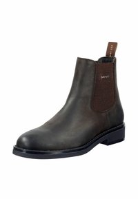 Bottine Chelsea en cuir marron avec des panneaux élastiques sur les côtés, bout rond, et une languette texturée à l'arrière. Semelle en caoutchouc robuste avec des détails de couture discrets.