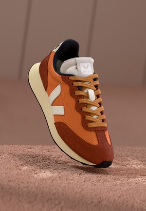 Orangene Netz- und Wildledersneaker mit cremefarbenen Akzenten und braunen Schnürsenkeln. Runde Zehenpartie und gepolsterte Sohle, mit einem weißen Logo auf der Zunge.