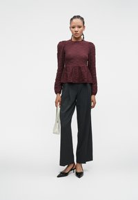 Top texturizzato color bordeaux con vita a peplum, maniche lunghe; abbinato a pantaloni grigi a vita alta e décolleté neri a punta; borsa bianca.