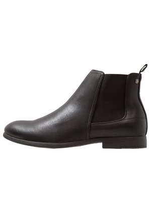 Bottine Chelsea en cuir noir à enfiler avec panneau latéral élastique, talon bas et languette de tirage sur fond blanc.