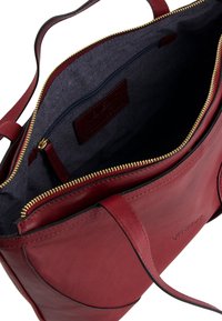 Red leather handbag with gold zipper, featuring a navy interior lining, logo tag, and a spacious main compartment with a zip pocket.