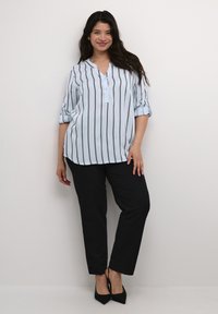 Blouse rayée bleu clair avec un col henley à bouton, manches retroussées, associée à un pantalon noir bien taillé et des escarpins noirs à bout pointu.