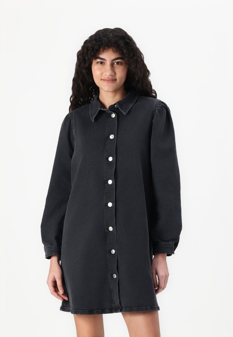 Rochie din denim negru cu închidere cu nasturi, guler și mâneci lungi cu manșete strânse. Textură netedă cu detaliu de cusătură subtil.
