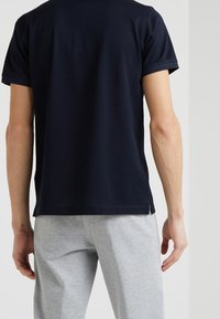 Marinblå t-shirt med kort ärm, tillverkad av bomull och har en rak passform med sidslitsar vid fållen. Bärs med gråa sweatpants.