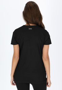 T-shirt nera in cotone con maniche corte e scollatura rotonda. Presenta un piccolo logo etichetta vicino alla parte superiore della schiena. Texture liscia.