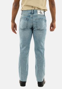 Jeans in denim azzurro chiaro con taglio dritto, tasche posteriori e etichetta di marca in vita. Il tessuto appare leggermente invecchiato.