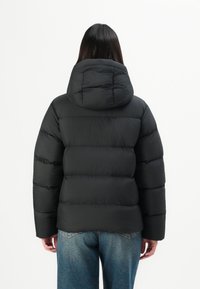 Black puffer jacket with a hood, featuring quilted sections and a soft texture. The design is simple, with long sleeves and a relaxed fit.