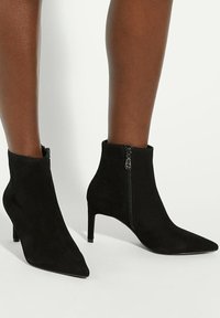 Black suede ankle boots with a pointed toe and a slim heel. Features a side zipper and smooth texture, offering a streamlined silhouette.