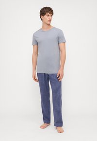 Camiseta cinza de algodão combinada com calças de pijama azuis com padrão de xadrez. As calças apresentam um padrão quadriculado e um corte descontraído, com uma textura macia.