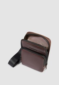 Borsa a tracolla in pelle marrone con due scomparti con zip, una tracolla nera e una texture liscia. Forma compatta con dettagli di design minimalisti.
