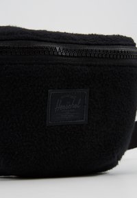 Czarna torba na ramię z flauszu o teksturowanej powierzchni, wyposażona w zamek błyskawiczny, regulowany pasek oraz czarną metkę z logo marki.