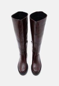 Ceļgalu augstumā burgundijas krāsas zābaki, izgatavoti no glancēta, teksturēta materiāla ar krokodila rakstu, ar taisnu zoli un noapaļotu purngalu.