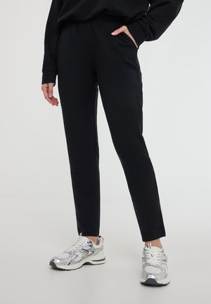 Czarne dresy o fakturowanym wykończeniu, z luźnym krojem, elastycznym paskiem i dekoracyjnymi ćwiekami przy kieszeniach. W połączeniu z srebrnymi sneakersami.