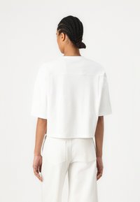 Afgebroken wit t-shirt van zacht katoen, met korte mouwen, een ronde hals en een gladde textuur, gecombineerd met witte wijde broek.