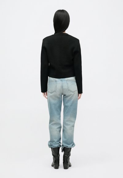 Κοντό μαύρο πουλόβερ φτιαγμένο από υφή υφάσματος, συνδυασμένο με ανοιχτό μπλε tapered τζιν. Οι μπότες είναι μαύρες με ελαφρώς υψωμένο τακούνι.