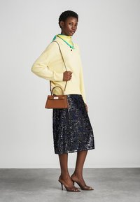 Suéter amarillo claro con cuello verde, combinado con una falda de lentejuelas azul marino. Un bolso marrón con un broche plateado y unos tacones altos completan el atuendo.