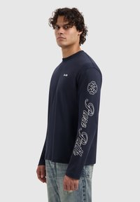 Navyblauwe longsleeve shirt van katoen met een ronde hals, voorzien van witte tekst "Pure Path" op de mouw en een logo op de borst.