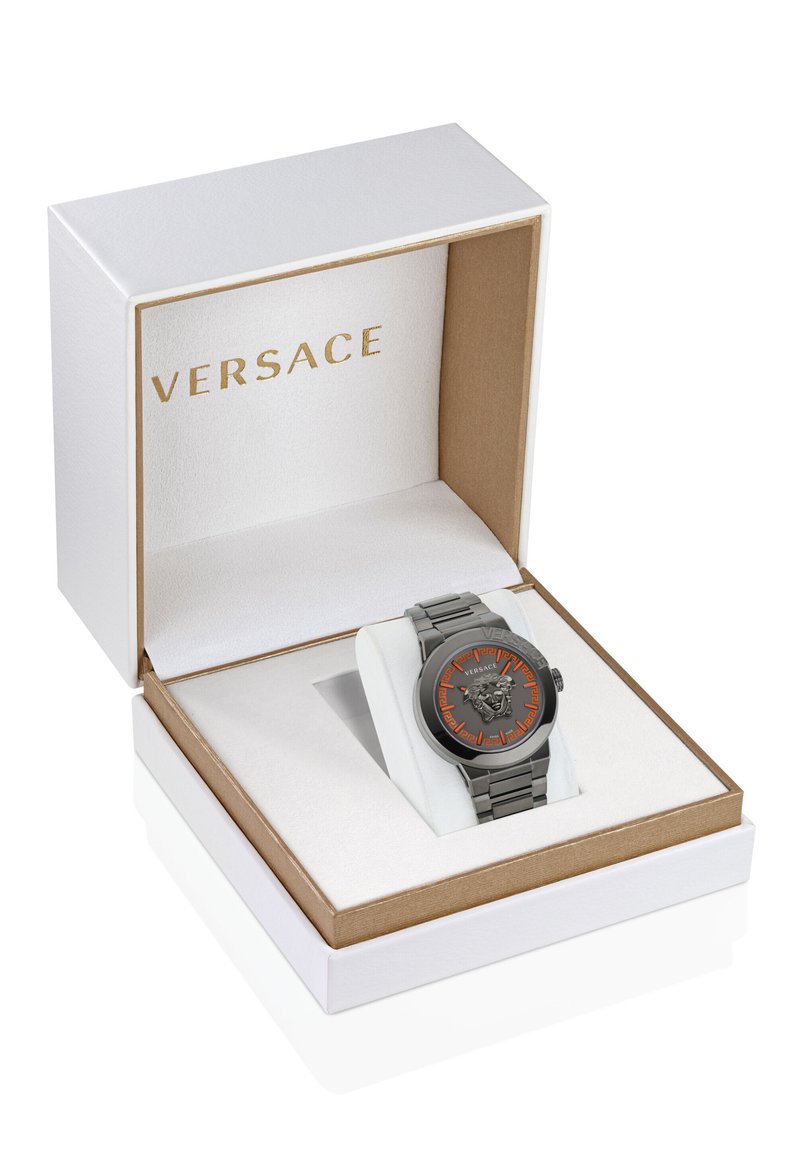 Orologio Versace in metallo grigio con quadrante arancione a motivo e emblemma del leone, esposto in una confezione regalo bianca e dorata con interno morbido.