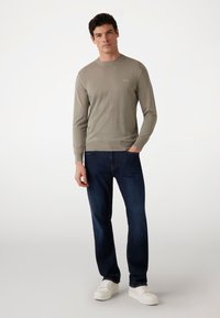 Lichtgrijze, lange mouwen trui met geribde kraag en boorden, gecombineerd met donkerblauwe jeans en witte sneakers. Eenvoudig, casual gebreid design.