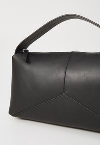Sac en cuir noir avec un design géométrique, doté d'un corps plat, d'une fermeture à zip et d'une large bandoulière pour le porter.