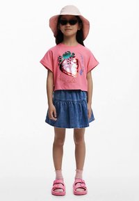 Pink színű crop top flitteres eper mintával, farmer szoknyával párosítva. Egy rózsaszín szandál és egy világos rózsaszín vödörkalap teszi teljessé az összeállítást.