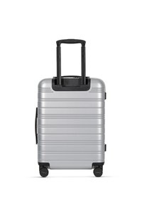Silberner Hartschalenkoffer mit horizontalen Rillen, schwarzem Griff und Rädern. Verfügt über einen ausziehbaren Griff und einen Seitengriff für einen einfachen Transport.