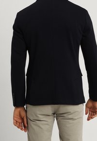 Blazer da uomo in navy, realizzato in tessuto testurizzato, con vestibilità su misura, due tasche frontali e uno spacco singolo sul retro.