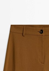 Bruine broek van gladde stof, met een knoopsluiting, een vlakke tailleband en subtiele diagonale stiksels vlakbij de zakken.