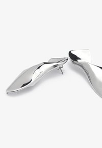 Metalliske sølvskohæler med et glatt, buet design. Har en spiss tå og en strømlinjet profil, som reflekterer lys med en polert overflate.