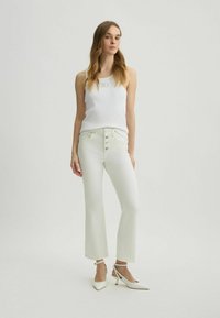 Top con spalline bianco a coste, jeans bianchi a vita alta con dettagli a bottone e décolleté bianchi con punta a sgancio. Texture liscia, design aderente.