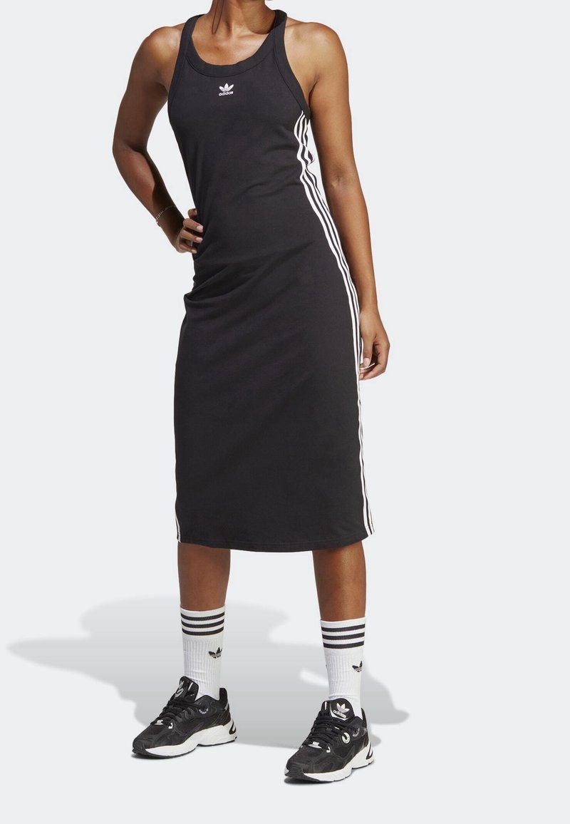 Zwarte mouwloze jurk met witte zijkanten, gemaakt van katoen. Model draagt zwarte sportschoenen en gestreepte sokken met logo-accenten.