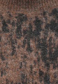 Kötött anyag, amely texturált mintázattal rendelkezik, földszínekben: barna, fekete és szürke, puha, bolyhos szálakkal és meleg megjelenéssel.