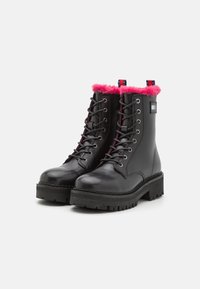 Botas negras de cuero con cordones, suelas resistentes y un brillante ribete de piel de color rosa alrededor de la parte superior, que cuentan con un pequeño parche de marca en el costado.