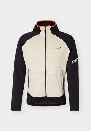 Giacca con cappuccio beige e nera con zip, rifiniture arancioni, logo sul petto e scritta "DYNA" sulla manica destra.