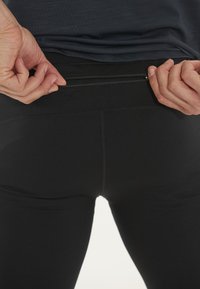 Svarta träningstights med en slät yta och ett litet dragkedjeförsett ficka på baksidan. En figurnära design förbättrar rörligheten under aktiviteter.